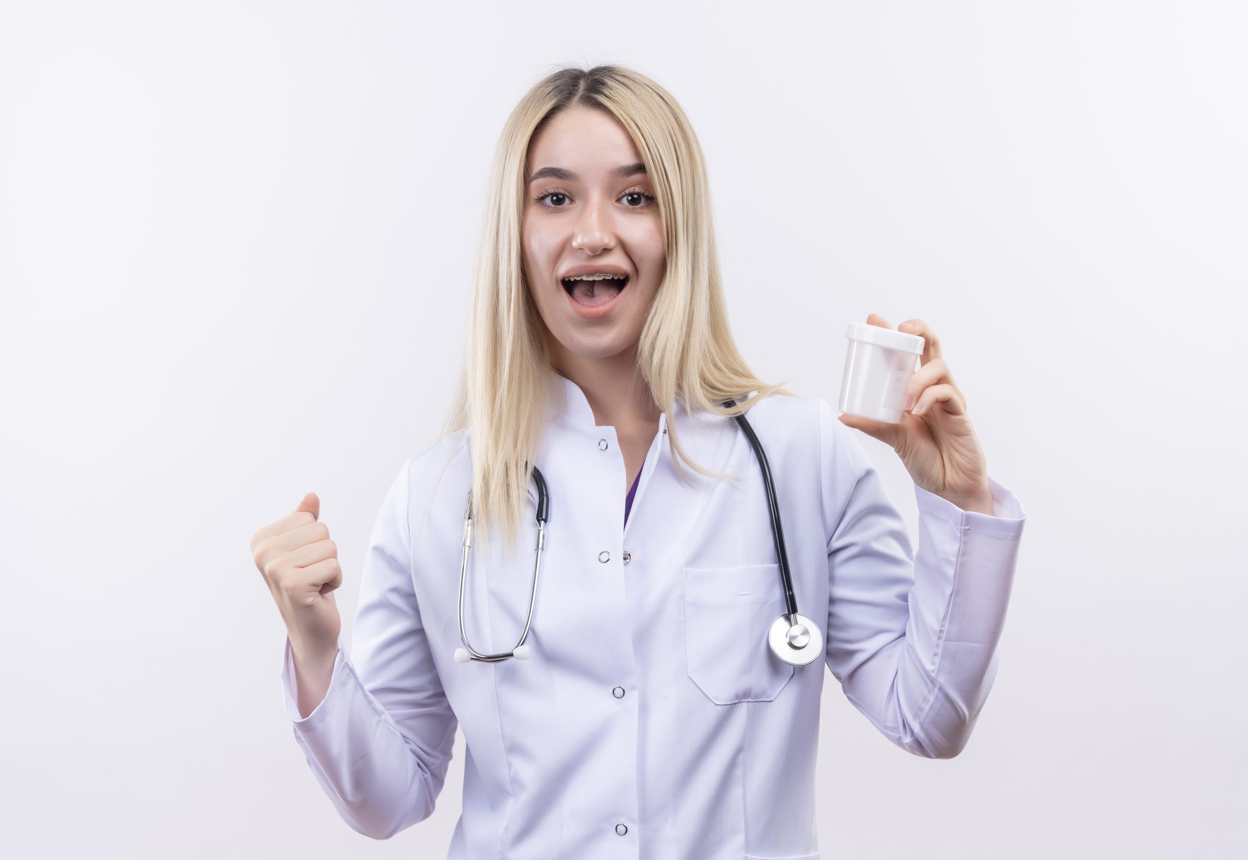 joyful doctor young blonde girl wearing stethoscope and medical gown in dental brace holding empty can showing yes gesture on isolated white background